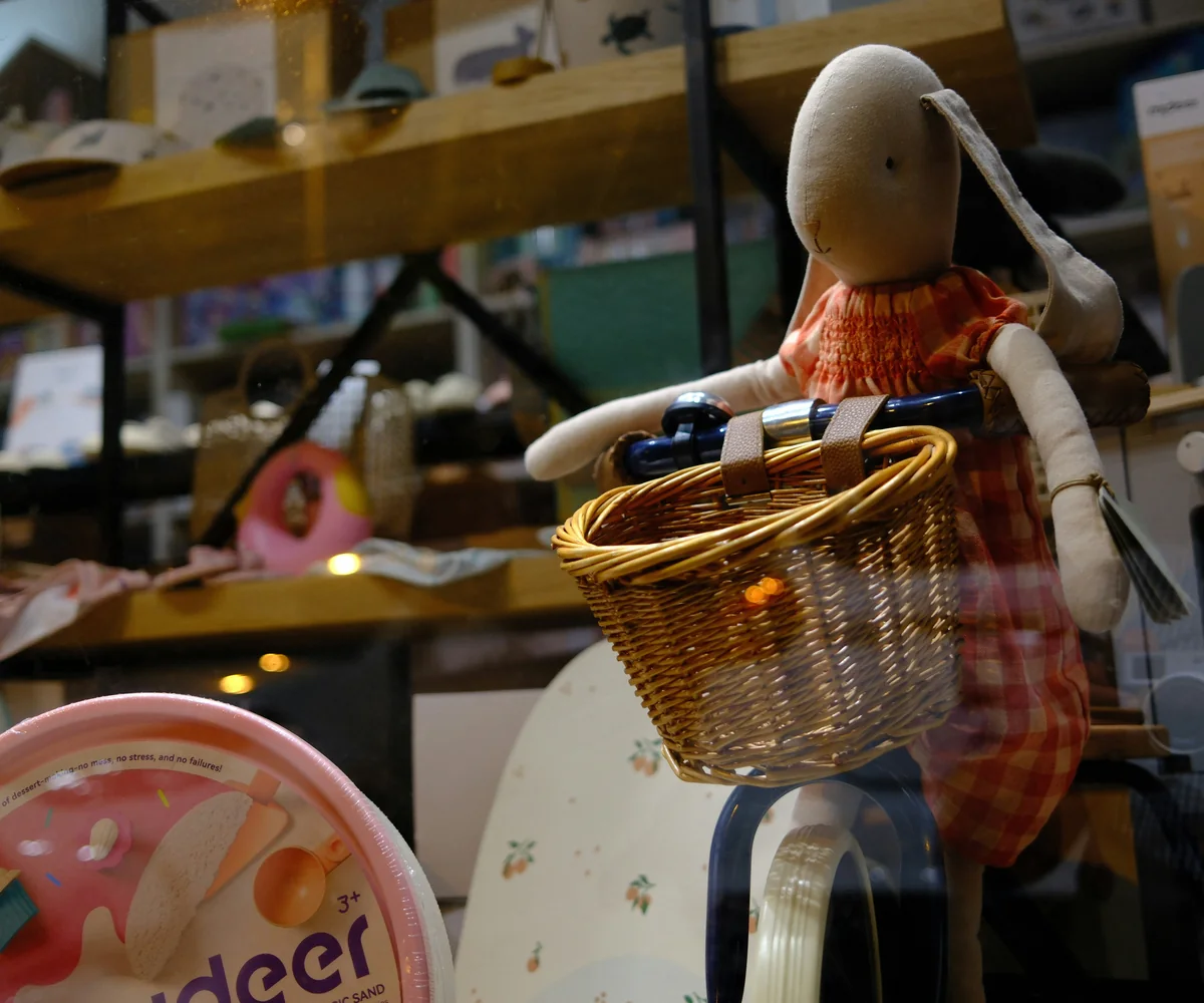 Handmade fabric doll carrying a wicker basket in a workshop setting.