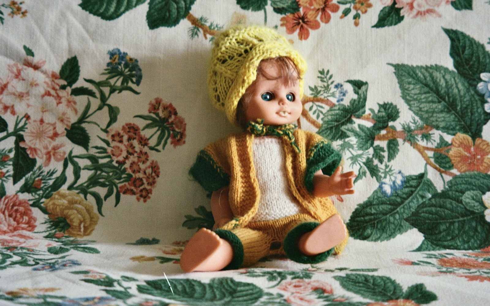 Close-up of a hand sewing vintage fabric with fine needle and thread, doll costume pieces laid out on a worktable.