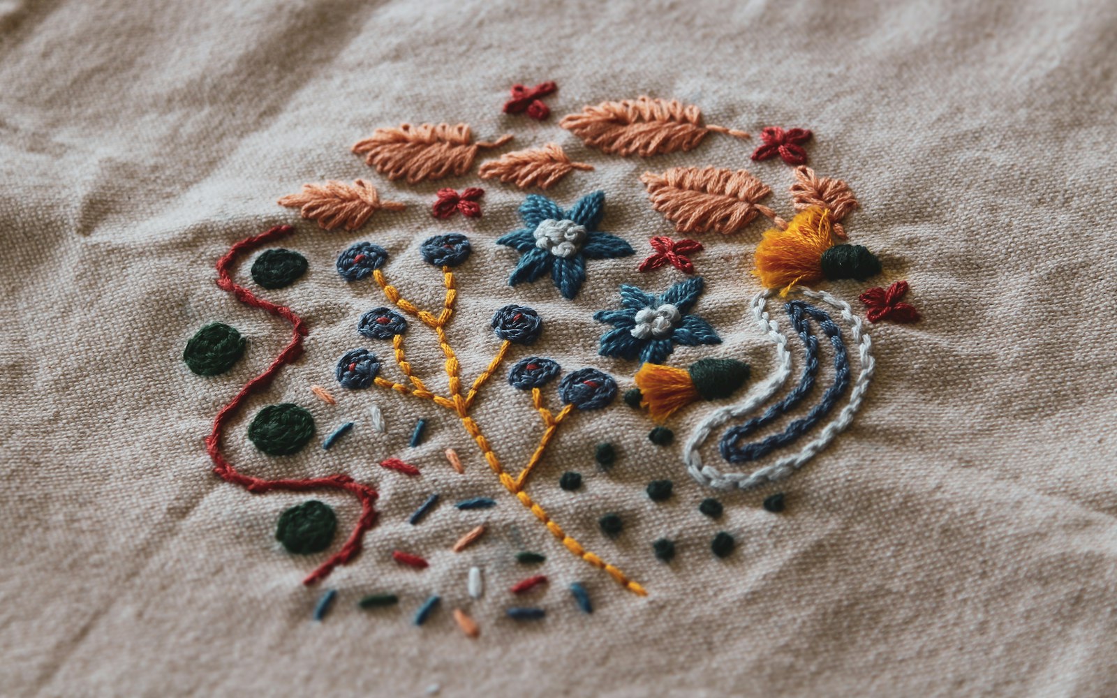Close view of hands adding fine embroidery to a flat fabric doll pattern piece beside thread, needles, and a small hoop.