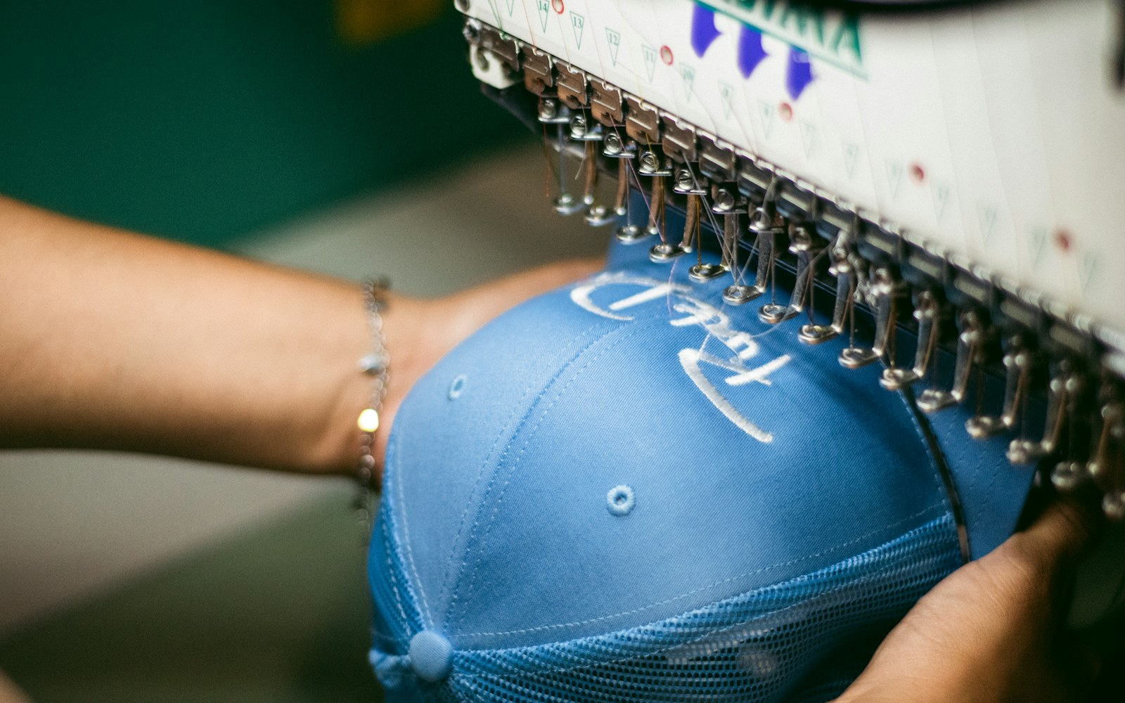 Close view of hands transferring a small embroidery motif onto pale fabric beside fine thread, a needle, and miniature doll clothing pieces.