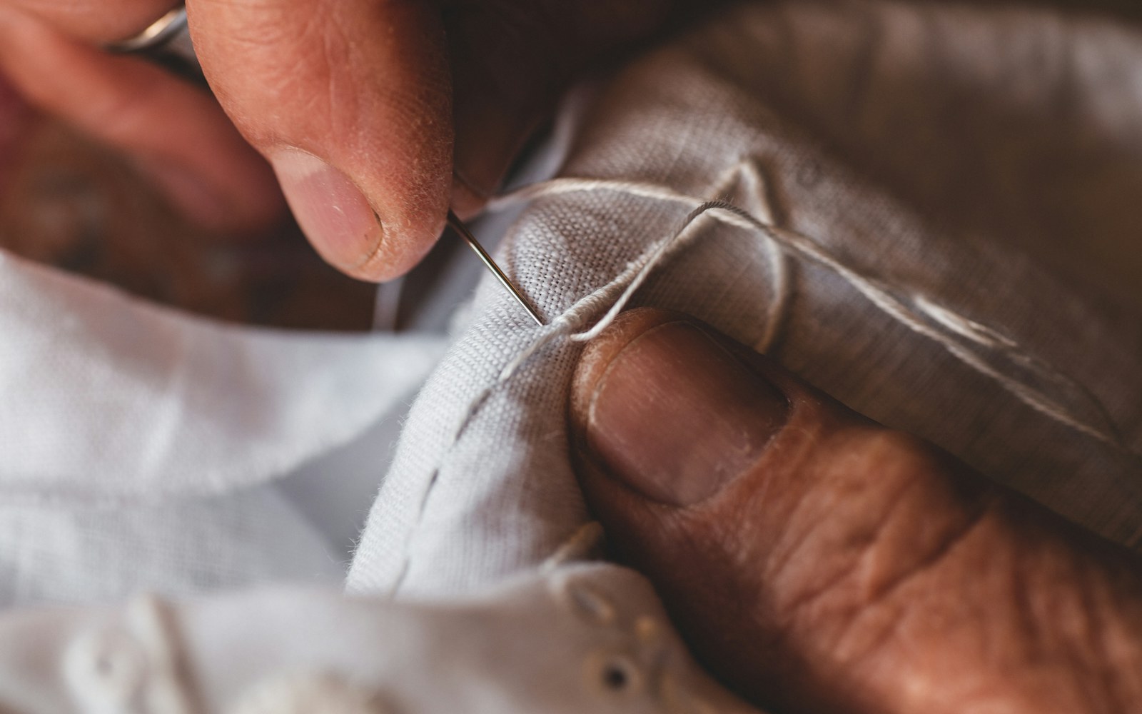 Close view of hands using a needle and matching thread to carefully repair the mouth seam of a handmade plush figure.