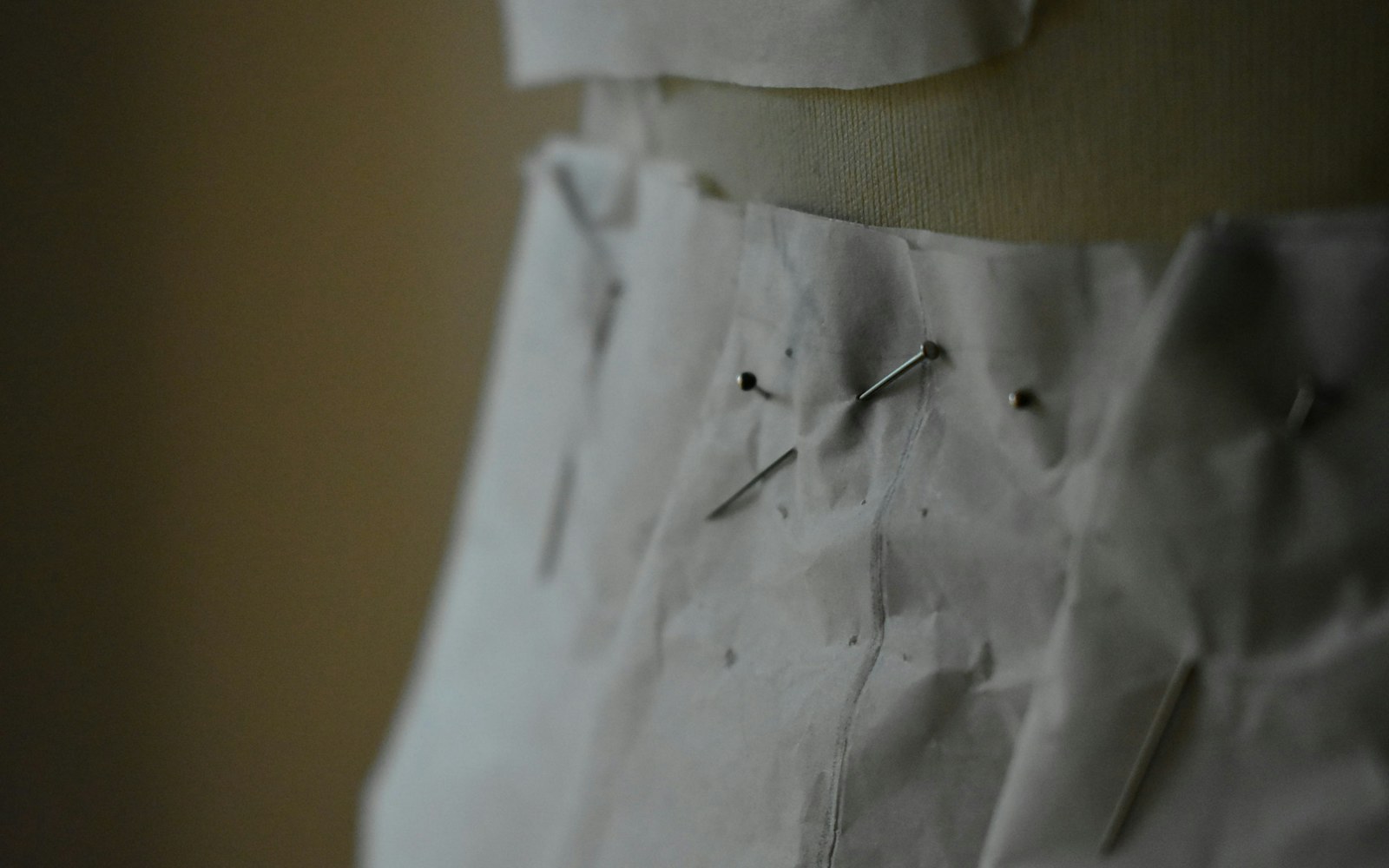 Close-up of a doll dress pattern pieces pinned to fabric on a worktable, with measuring tape and scissors nearby.