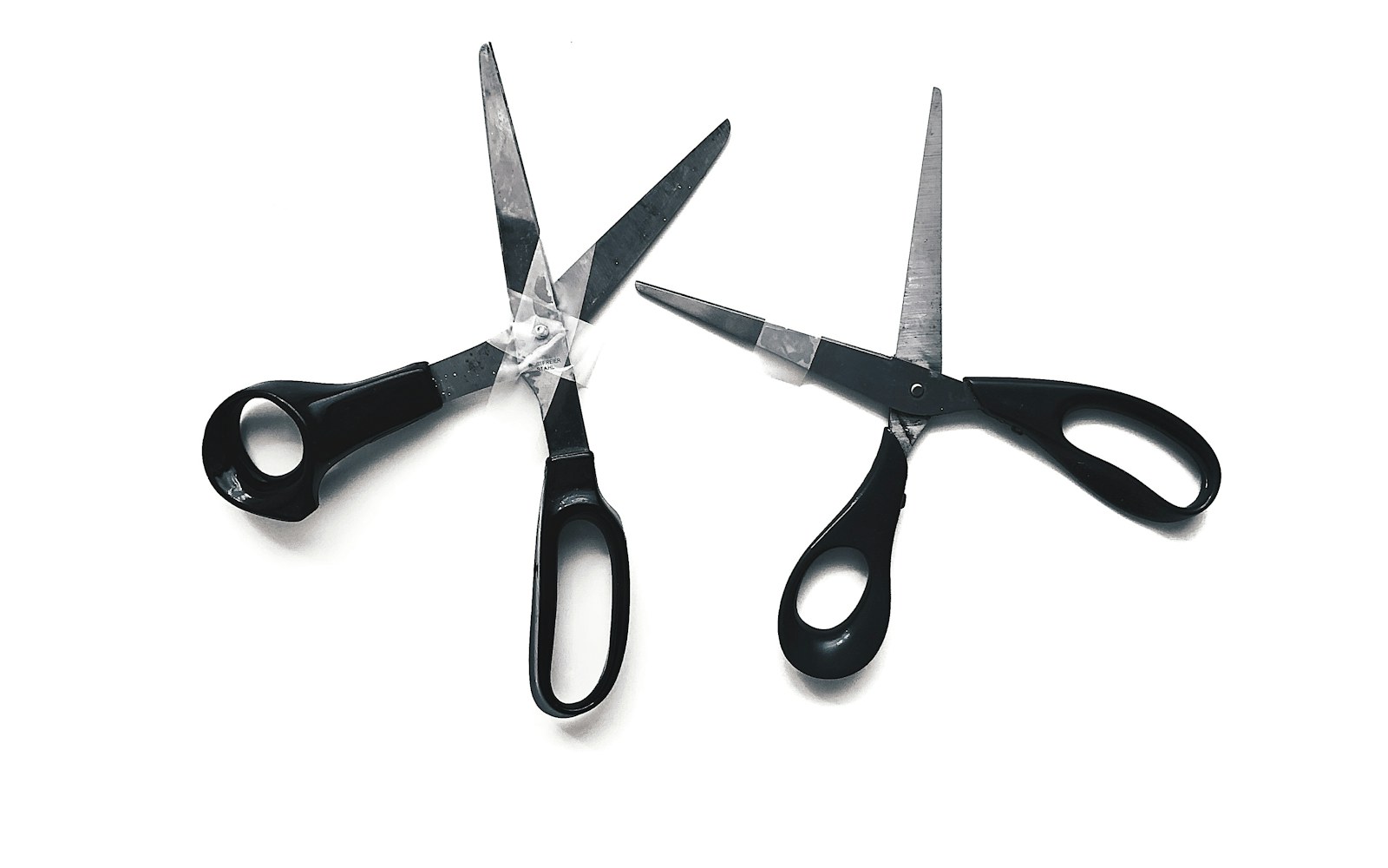 An assortment of scissors for doll making laid out on a wooden table, including large fabric shears, small embroidery scissors, and fine micro-tip snips, with threads and fabric scraps nearby.