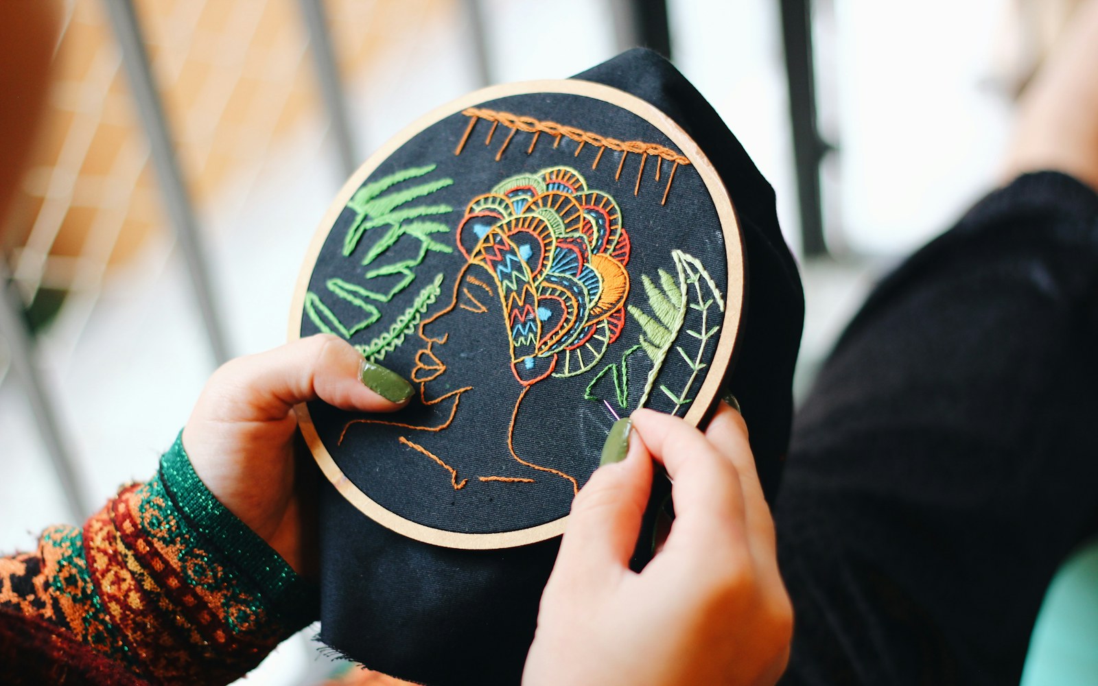 Close-up of embroidering a marked cloth doll face in a small hoop, with thread and needle nearby.