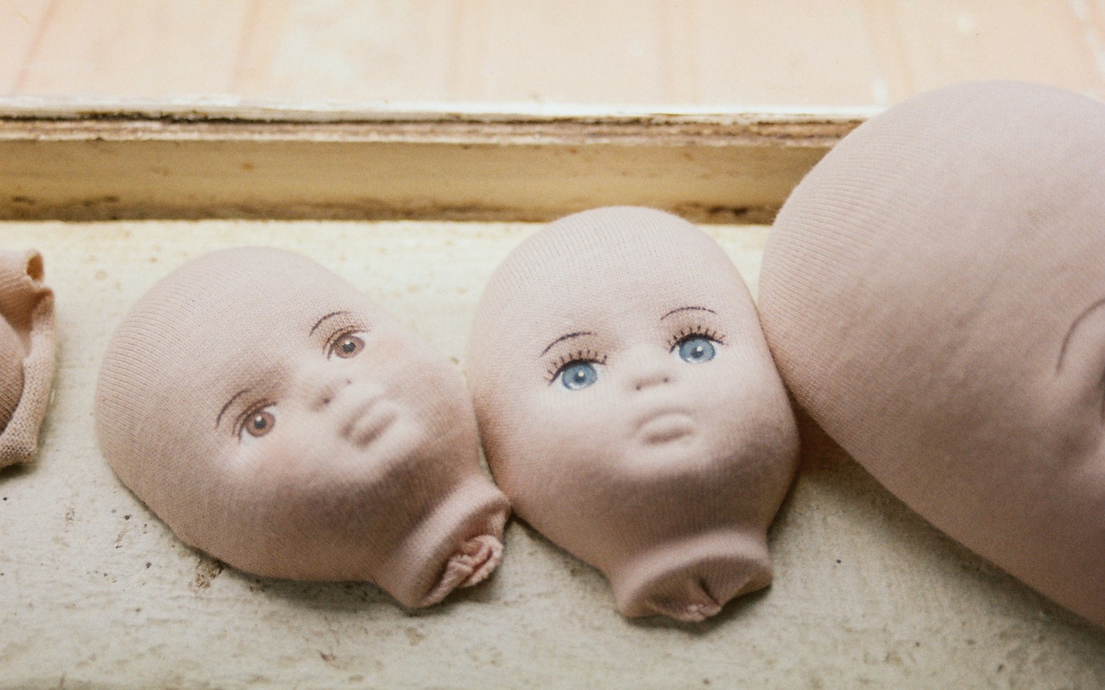Close-up of a doll maker's hands carefully applying a thin coat of clear glaze to a polymer clay face with a fine brush, surrounded by test scraps and a clean work surface.