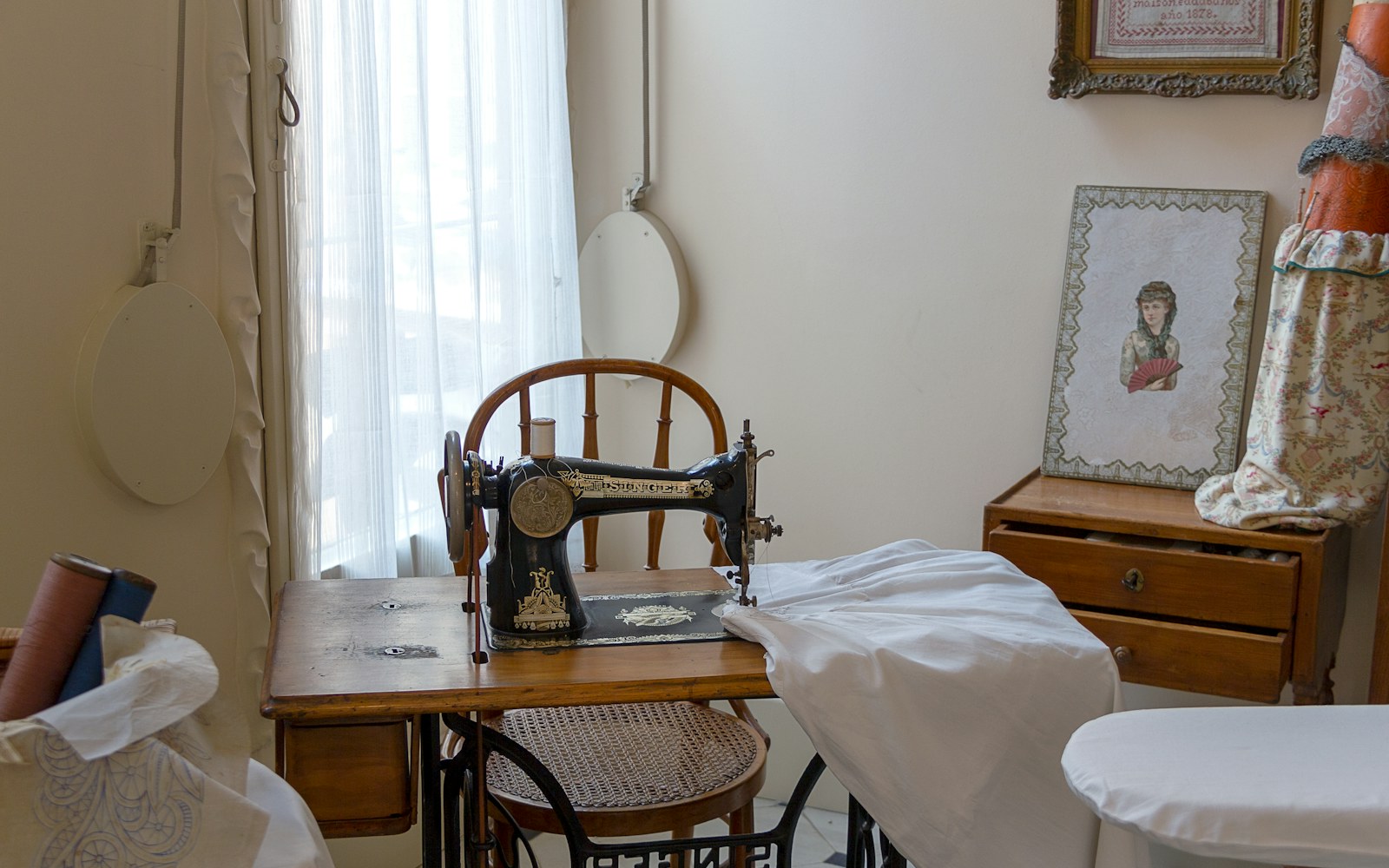 A sewing machine with tiny doll clothing pieces on the sewing table