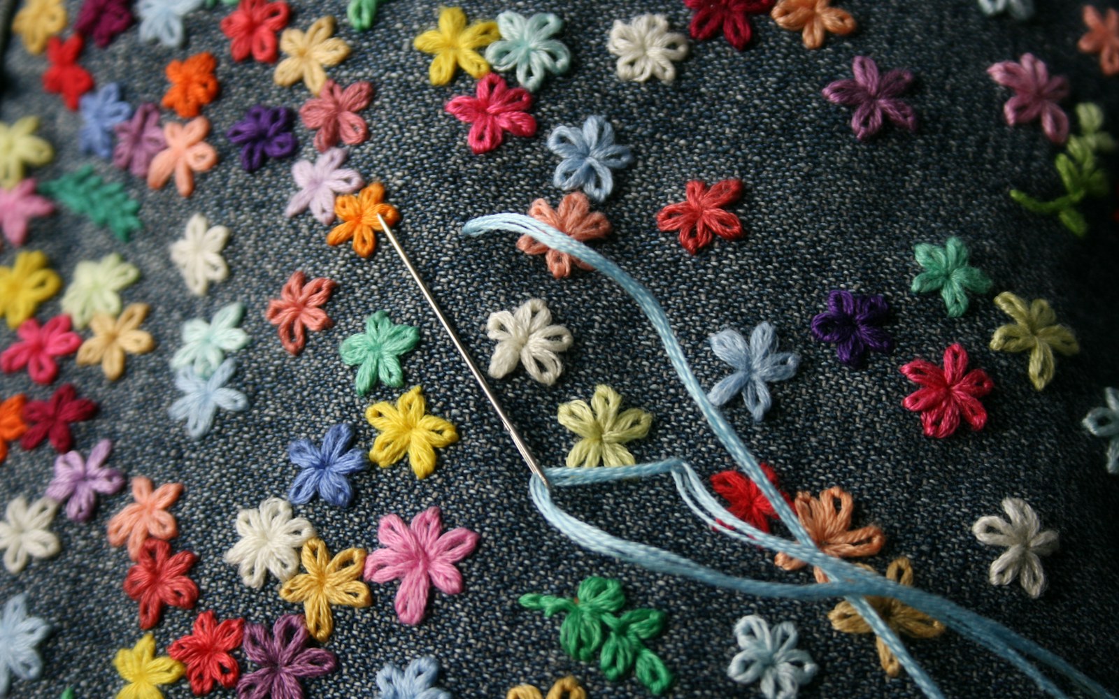 Close view of a handmade textile doll armature wrapped in thread and batting beside silk fabric, embroidery floss, wire cutters, and small stitched wings.